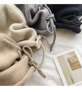 Detail of chunky knit beanies in beige, grey, and black with matching drawstrings