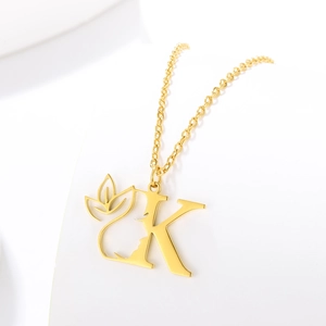 Macro view of gold-plated letter K pendant with hollowed-out face silhouette and leaf detail