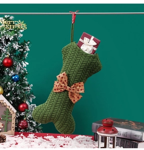 Detail of green bone-shaped knitted Christmas stocking with large polka dot bow on tree
