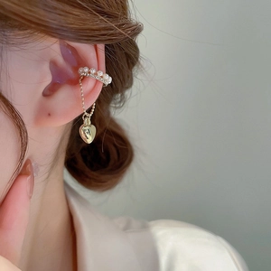 Detail of gold ear cuff featuring white pearls and a polished heart pendant on a thin chain