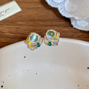 Macro shot of gold floral earrings with green opal, white pearls and sparkling crystals