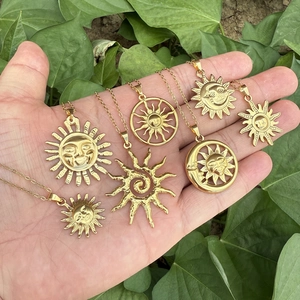 Collection of seven golden stainless steel sun pendant necklaces held on a palm with green leaves