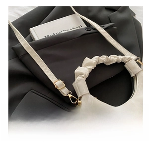 Close-up of white cloud bag with pleated handle and gold adjustable buckle on dark fabric