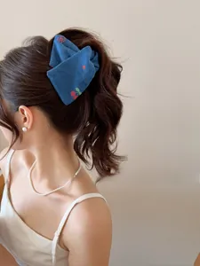 Détail d'un nœud papillon en denim bleu avec broderie cerise sur la queue de cheval du modèle