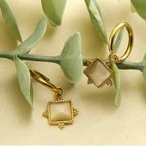 Close-up of gold square opal earrings with beaded edges on a textured fabric