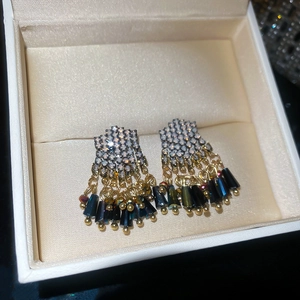 Detail view of gold tassel earrings with crystal studs and dark blue beads in a jewelry box
