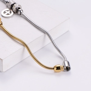 Close-up of dual-tone snake chain bracelet featuring a cross pendant and crystal spacers