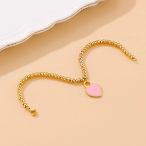 Beaded 18k gold plated titanium bracelet with a pink enamel heart pendant on beige surface