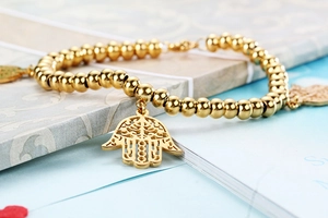Macro shot of gold beaded elastic bracelet with Hamsa Hand charms in polished finish