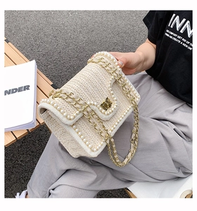 Detailed view of pearl-trimmed woven straw crossbody bag with golden chain strap