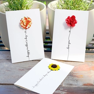 Three handmade dried flower greeting cards with warm messages on a wooden surface