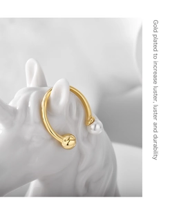 Detailed view of a gold-plated ear cuff with pearl on white ceramic horse head