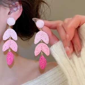 Macro view of pink raffia fringe earrings with woven texture and gold metal rings