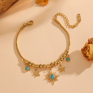 Gold celestial snake chain bracelet with turquoise sun and star charms on beige background
