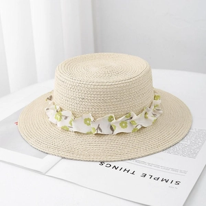 Flat top straw boater hat with floral ribbon on beige woven texture for beach