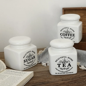 Three-piece set of white ceramic storage jars for sugar, tea, and coffee on wooden surface