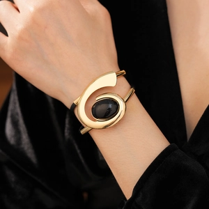 Close-up of a gold double-layer oval bracelet featuring a black gemstone on wrist