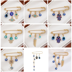 Golden Hamsa hand and blue evil eye brooch pins set with crystals and tassels