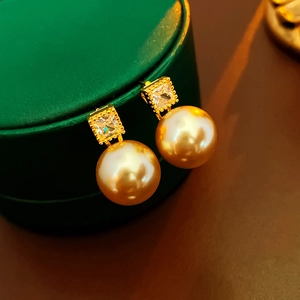 Detail of gold plated earrings featuring square zircon and round pearls on jewelry box