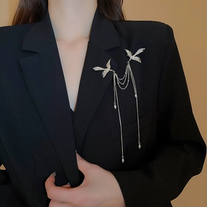 Dettaglio della spilla a fenice d'argento con perle e nappe su un blazer nero elegante