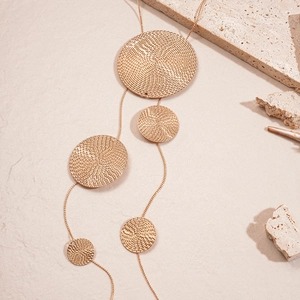 Macro detail of golden round metal pendants with spiral texture on long sweater necklace