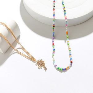 Detail view of gold palm tree pendant necklace and colorful beaded strand on white cubes