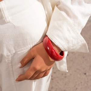 Detail of chunky bold red resin geometric bangle on model with white linen background