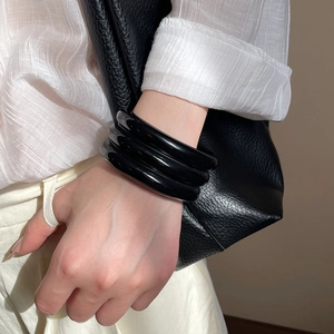 Detail of three-layer black resin geometric bangles worn with a white shirt