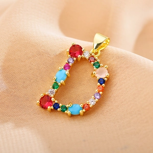 Close-up of golden letter D pendant set with colorful zircon stones on beige fabric