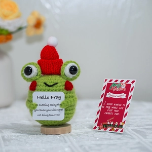 Detailed view of a handmade crochet Christmas frog doll with a card on a wooden base