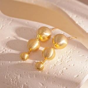 Macro shot of gold matte graduated triple ball earrings on a white stone background