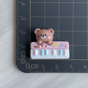 Detail shot of a 2cm resin brown bear on a pink piano keyboard charm for DIY crafts