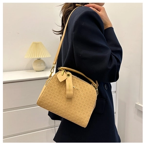 Close-up of beige woven shell bag featuring leather handles and brand name tag detail