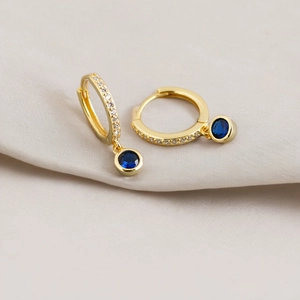 Macro shot of gold hoop earrings with micro-inlaid zircons and a round dark blue gemstone