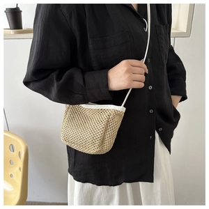 Dettaglio di una borsa a secchiello in paglia intrecciata indossata da una modella