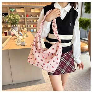 Pink corduroy shoulder bag with red strawberry print and ruffled strap on a model