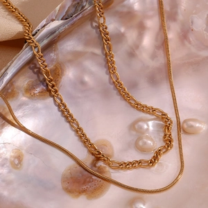 Detailed shot of double-layer gold necklace set with figaro and snake chains in a shell