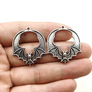 Detail of vintage bat pendants in antique silver finish held for scale on white background