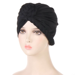 Dettaglio di un turbante nero con treccia laterale e fiore decorativo in tessuto sopra