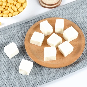 Miniature tofu model pieces displayed on a wooden tray with yellow soybeans in macro view
