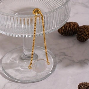 Detail of baroque pearl on golden box chain draped over textured glass for aesthetic display