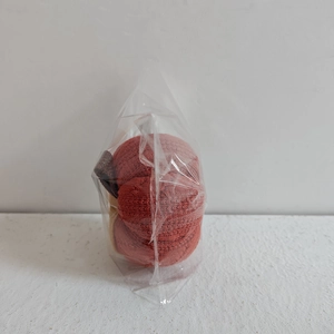 Macro detail of red knitted pumpkin ornament in plastic packaging for harvest decor