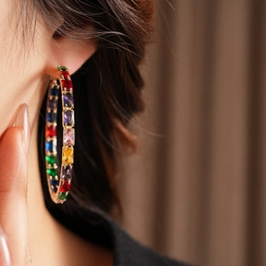 Close-up of gold hoop earrings with multi-colored rectangular crystals on model