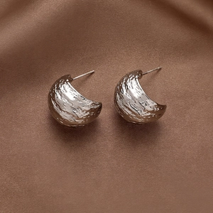 Detail view of silver C-shaped earrings with hammered texture on brown satin fabric