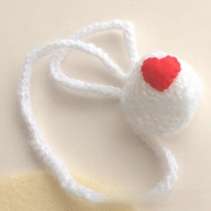 Detail showing a handmade white crochet nose warmer with a red heart charm and woven loop