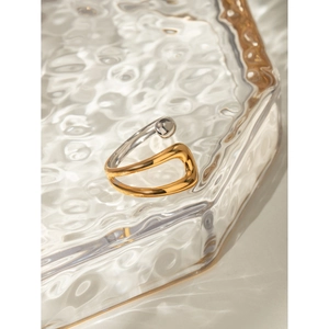Detail of bicolor gold and silver crossover open ring on a wavy glass tray