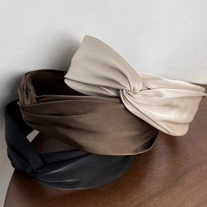 Detail of three satin twisted headbands in beige, brown, and black on a wooden surface