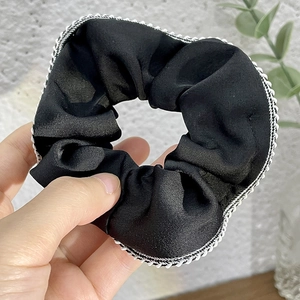 Elegant black satin scrunchie with white stitched edges and smooth pleated texture