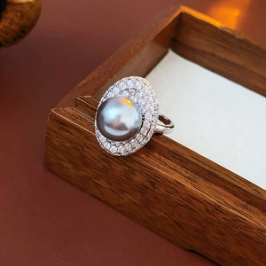 Close-up of a grey pearl ring with zircon halo on a dark wooden jewelry display stand