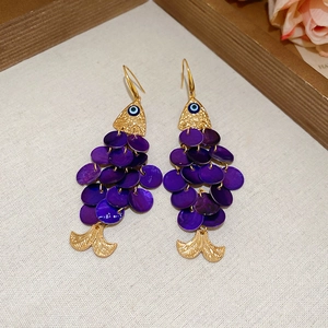 Detail of fish earrings with purple shells and blue evil eye accents on beige fabric